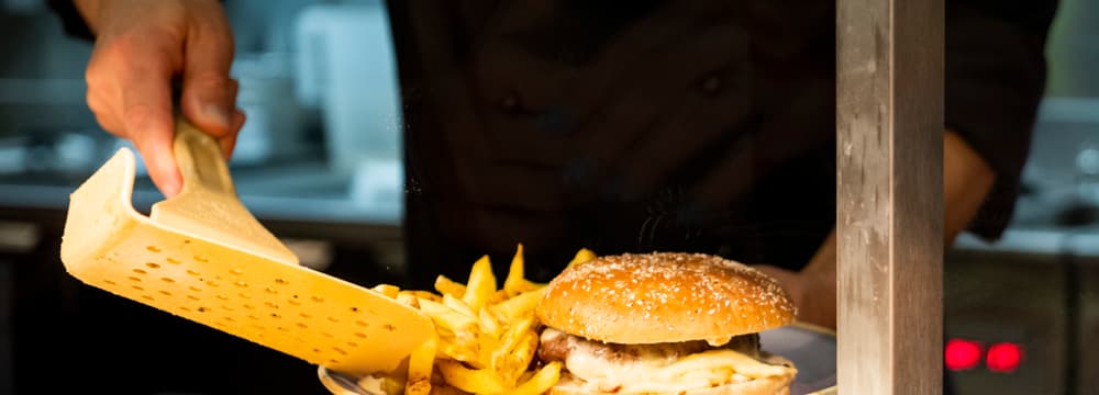 Ein Mitarbeiter schöpft im Zoorestaurant Pommes Frites auf einen Teller mit einem Hamburger.