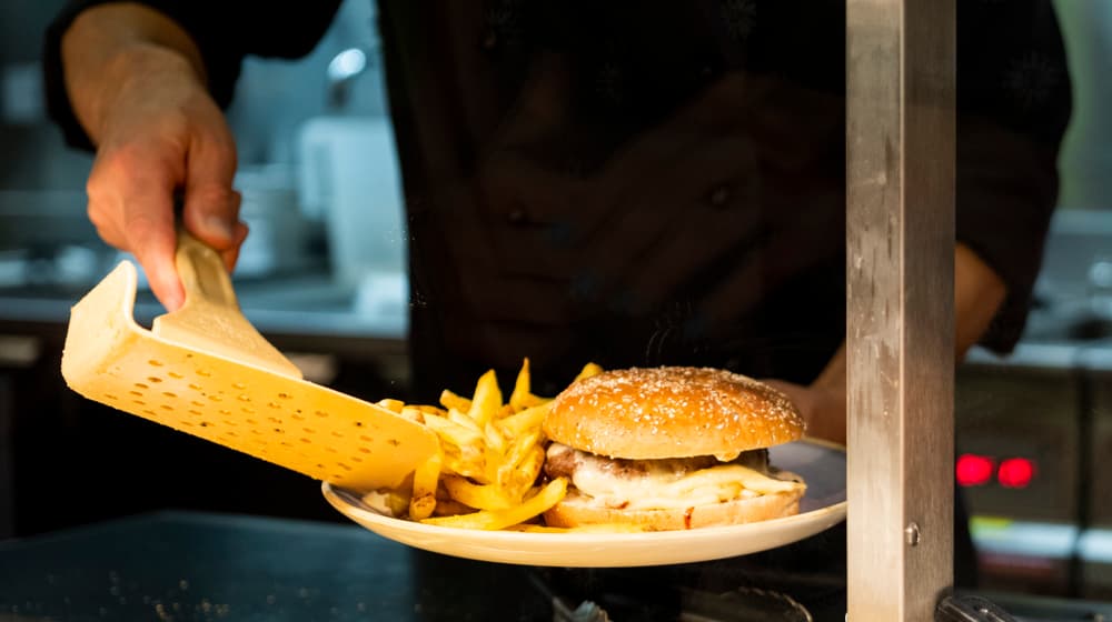 Ein Mitarbeiter schöpft im Zoorestaurant Pommes Frites auf einen Teller mit einem Hamburger.